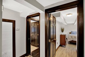 A hallway with wooden doors leading to a bedroom with a bed and a small cabinet. - Unique Downtown 2br 2ba close to everything Apt.B (Gainesville)