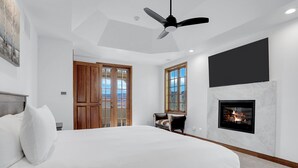 Une chambre à coucher avec un grand lit, un ventilateur de plafond, une cheminée et une vue sur l’extérieur par les fenêtres.