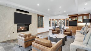 Ein modernes Wohnzimmer mit Ledersofas, einem Kamin, einem Flachbildfernseher und einem Essbereich mit Holzsäulen.