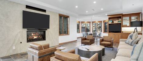 A modern living room with leather sofas, a fireplace, a flat-screen TV, and a dining area with wooden cabinets.