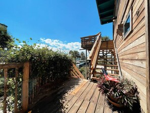 A wooden deck with a wooden staircase leading to a balcony, surrounded by greenery and a clear blue sky. - Penthouse Artist Haven Ocean front Penthouse (St. Augustine)