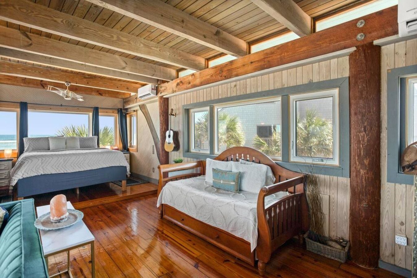 Une chambre confortable, aménagée dans le style d’un chalet, avec deux lits, un plancher en bois, de grandes fenêtres et une guitare.