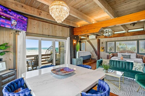 Een ruime kamer met een grote eettafel, comfortabele zitplaatsen, uitzicht op het strand en een gezellige zithoek met een gitaar.