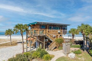 Ein Holzstrandhaus mit Balkon, gelegen an einem Sandstrand mit Palmen.
