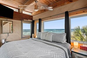 A bedroom with a large bed, wooden ceiling, and a view of the ocean.