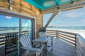 A wooden deck with a table and chairs overlooking a beach.