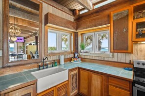 A kitchen with wooden cabinets, a large sink, and a view of the ocean through windows. - Penthouse Artist Haven Ocean front Penthouse (St. Augustine)