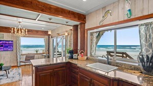 A kitchen with wooden cabinets, a granite countertop, and a view of the beach. - Treehouse Artist Haven Direct Oceanfront 2br (St. Augustine)