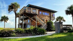 A wooden house with a balcony, surrounded by palm trees and a grassy area. - Treehouse Artist Haven Direct Oceanfront 2br (St. Augustine)