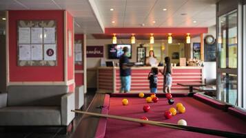 Een pooltafel met ballen, een zithoek en een bar met mensen op de achtergrond.