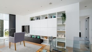 Un salon moderne avec un canapé gris, une table basse en verre et un meuble de rangement blanc doté d’étagères.