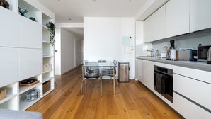 Une cuisine moderne avec des meubles blancs, un réfrigérateur en acier inoxydable et un coin repas comprenant une table et des chaises en verre.