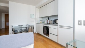 Une cuisine moderne avec des meubles blancs, une table à manger en verre et un four encastré.