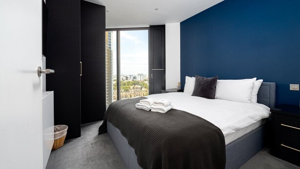 Une chambre d’hôtel moderne avec un grand lit, une vue sur la ville et un mur d’accent bleu foncé.