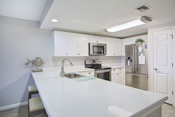 A modern kitchen with white cabinetry, stainless steel appliances, and a large island with a sink. - Amalfi Coast 427D - Beautiful Beach Views, Amazing Onsite Amenities! (Miramar Beach)