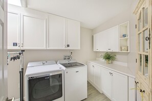 A laundry room with a front-loading washer and dryer, white cabinets, and a small shelf with a plant. - Amalfi Coast 427D - Beautiful Beach Views, Amazing Onsite Amenities! (Miramar Beach)