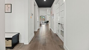 A modern hallway with white walls, a dark ceiling, and a wooden floor. There are framed pictures on the walls and a bench with baskets at the end.
