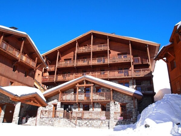 Un edificio de madera de varios pisos con balcones, base de piedra y acumulación de nieve.