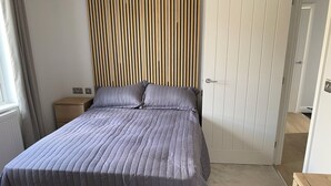 A neatly made bed with a striped bedspread, a wooden headboard, a bedside table, and a door in a room. - Tranquil Lodge Retreat in Wells (Wells)