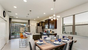 Una cocina moderna con armarios oscuros, una isla central y un comedor con mesa y sillas de madera.