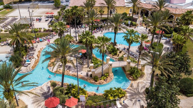A resort with a large swimming pool, palm trees, and a covered area with umbrellas.
