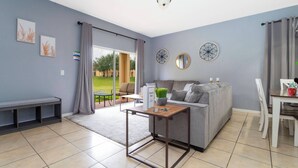 A modern living room with a grey sofa, a wooden coffee table, and a dining area with a white table and chairs.