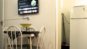 A small kitchen with a dining table and chairs, a TV mounted on the wall, and a refrigerator. - Apto 422 Ed. São Lucas (Praia Grande)