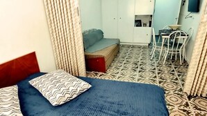 A bedroom with a bed, a sofa, a dining table with chairs, and a ceiling fan. - Apto 422 Ed. São Lucas (Praia Grande)