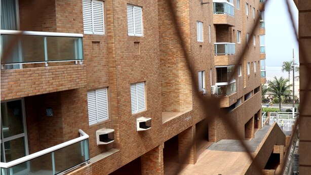 A multi-story brick building with balconies, air conditioning units, and a wooden deck. - Apto 422 Ed. São Lucas (Praia Grande)