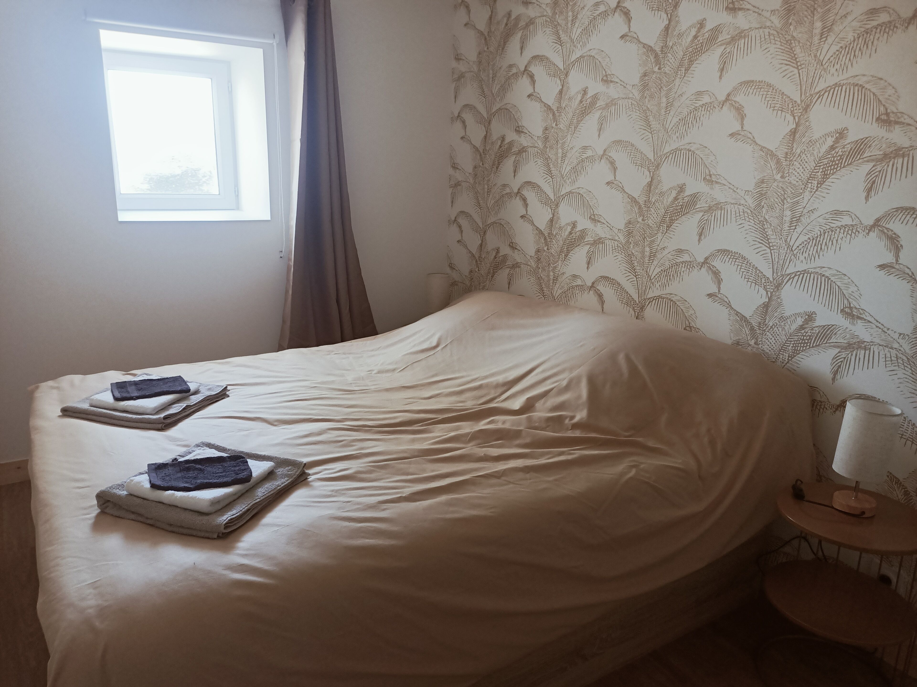 A neatly made bed with folded towels and a bedside table with a lamp.