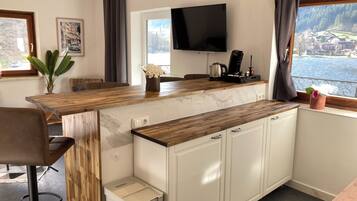 A modern kitchen with a wooden countertop, white cabinets, a built-in TV, and a view of a lake.