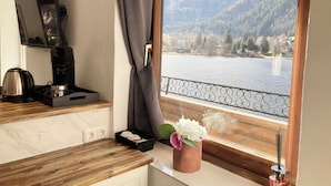 Una cocina con cafetera, hervidor y un florero junto a una ventana con vistas a un lago y montañas.