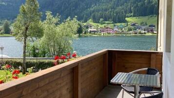 Un balcon avec vue sur un lac et des montagnes, une balustrade en bois et une table avec des chaises.
