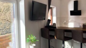 A modern kitchen with a flat-screen TV, bar stools, and a potted plant.
