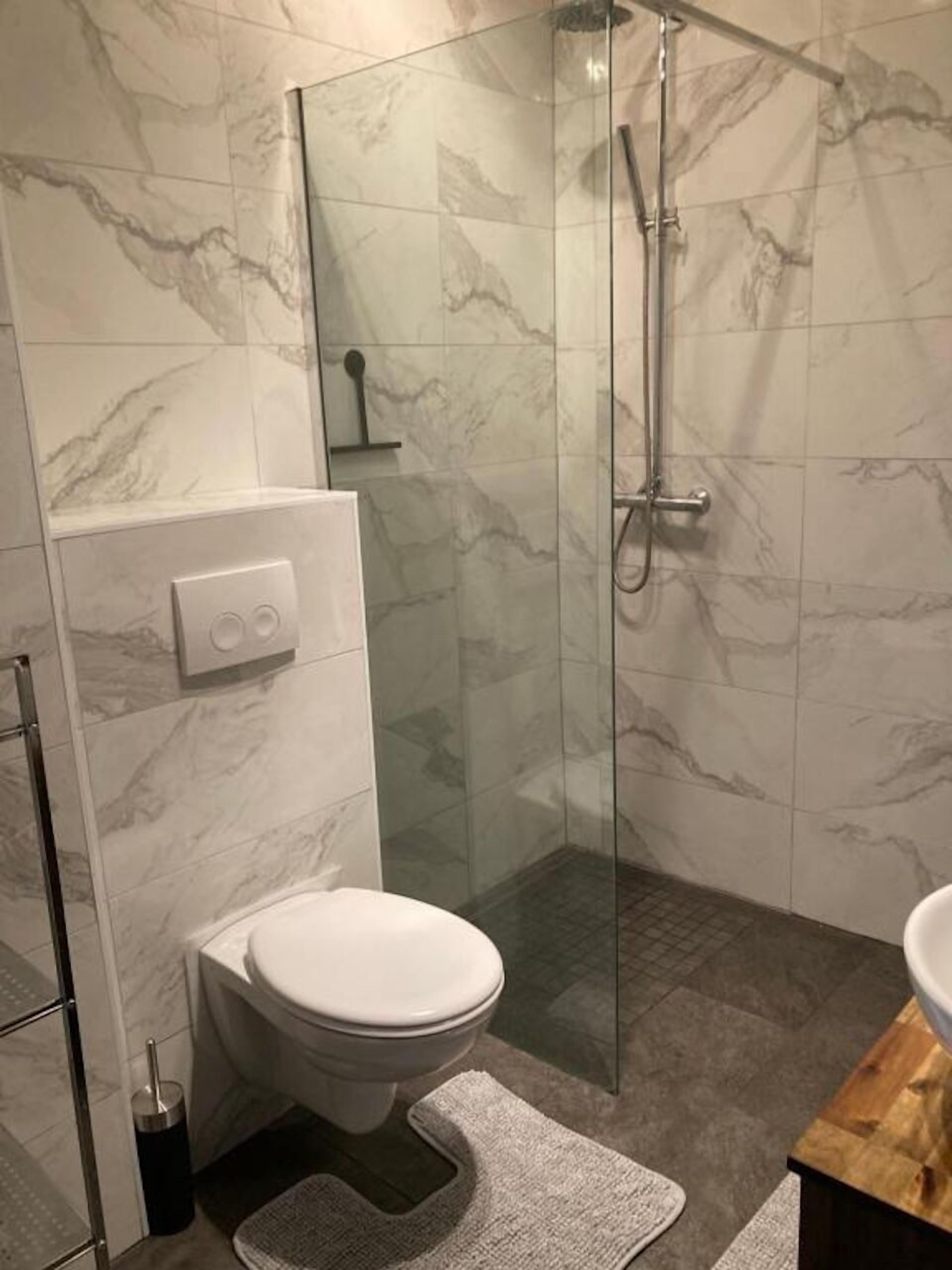 A bathroom with a toilet, a shower with a glass door, and marble tiles.