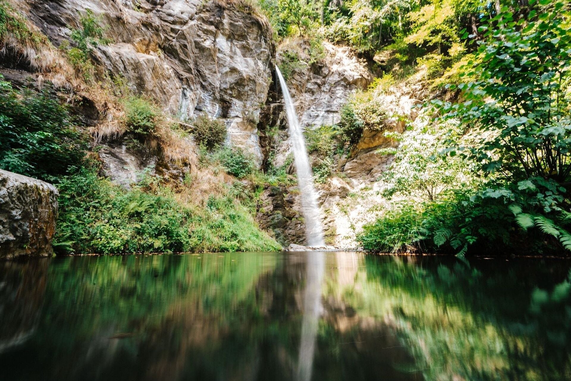 A waterfall cascading into a calm lake surrounded by rocky cliffs and lush greenery.