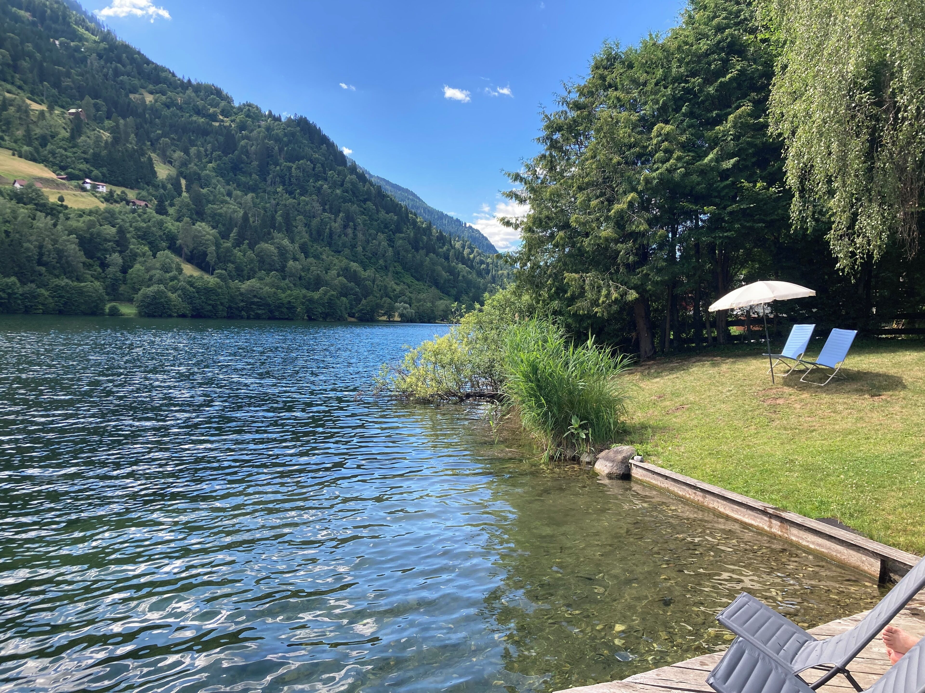 A lakeside view with a dock, a chair, and an umbrella.