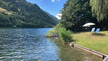 A lakeside view with a dock, a chair, and an umbrella.