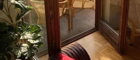 A room with a sliding glass door leading to an outdoor balcony with wicker chairs and a view of a river and mountains.