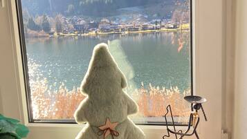A plush Christmas tree on a windowsill with a view of a lake and mountains.