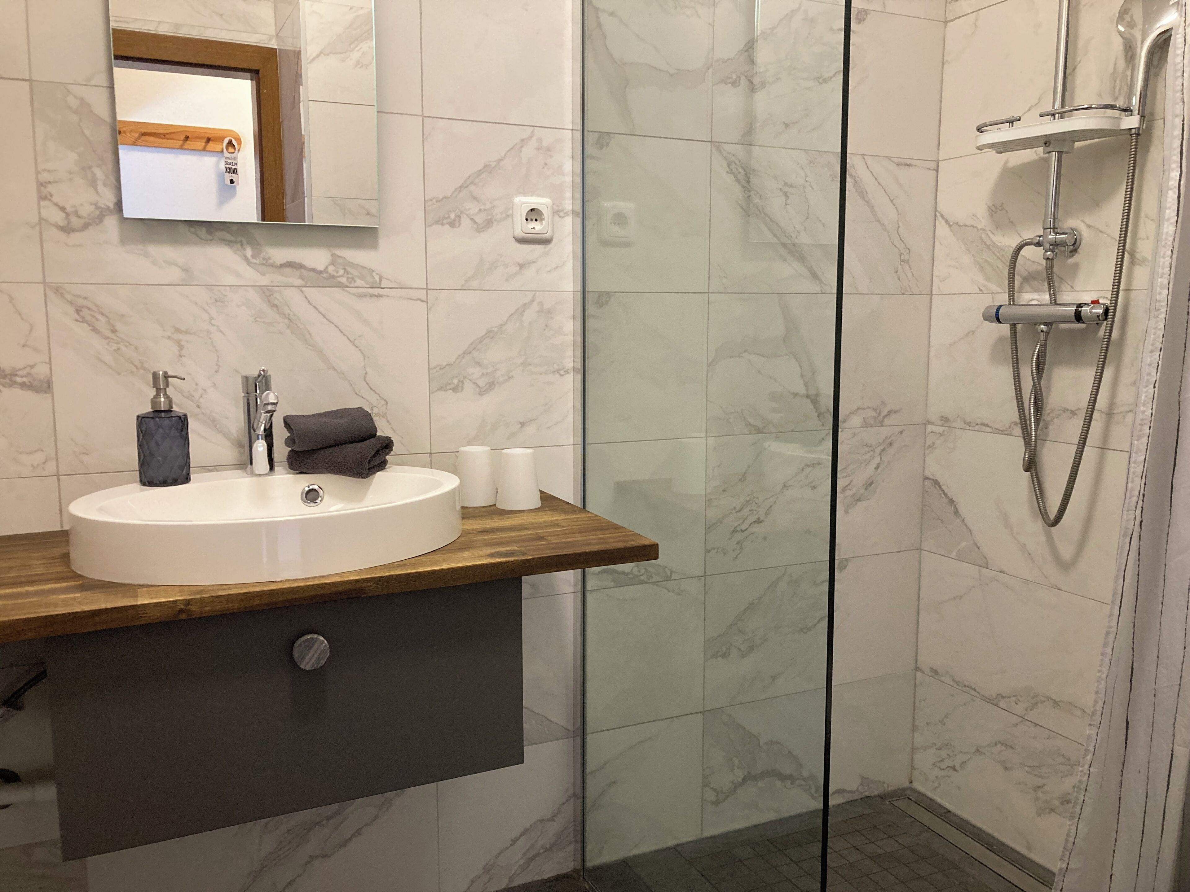 Une salle de bain moderne avec une douche carrelée de marbre, un meuble-lavabo en bois, un lavabo et un miroir.