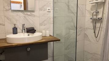 Une salle de bain moderne avec une douche carrelée de marbre, un meuble-lavabo en bois, un lavabo et un miroir.
