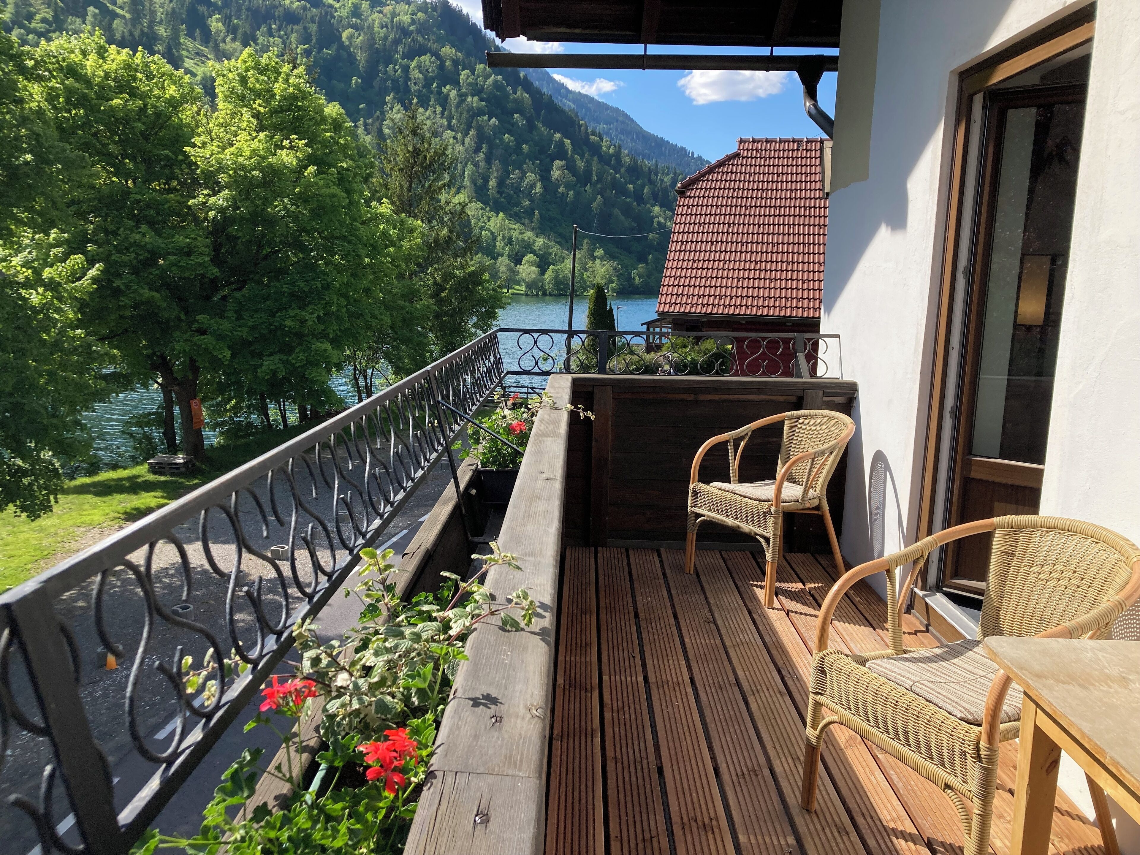 A wooden deck with wicker chairs overlooking a lake and forested mountains.