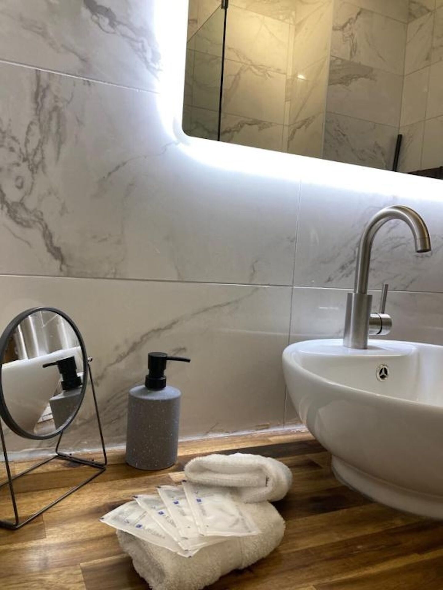 Un baño con salpicadero de mármol, un lavabo con grifo moderno, un espejo, un dispensador de jabón y una toalla en el suelo.