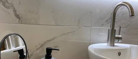 Un baño con salpicadero de mármol, un lavabo con grifo moderno, un espejo, un dispensador de jabón y una toalla en el suelo.