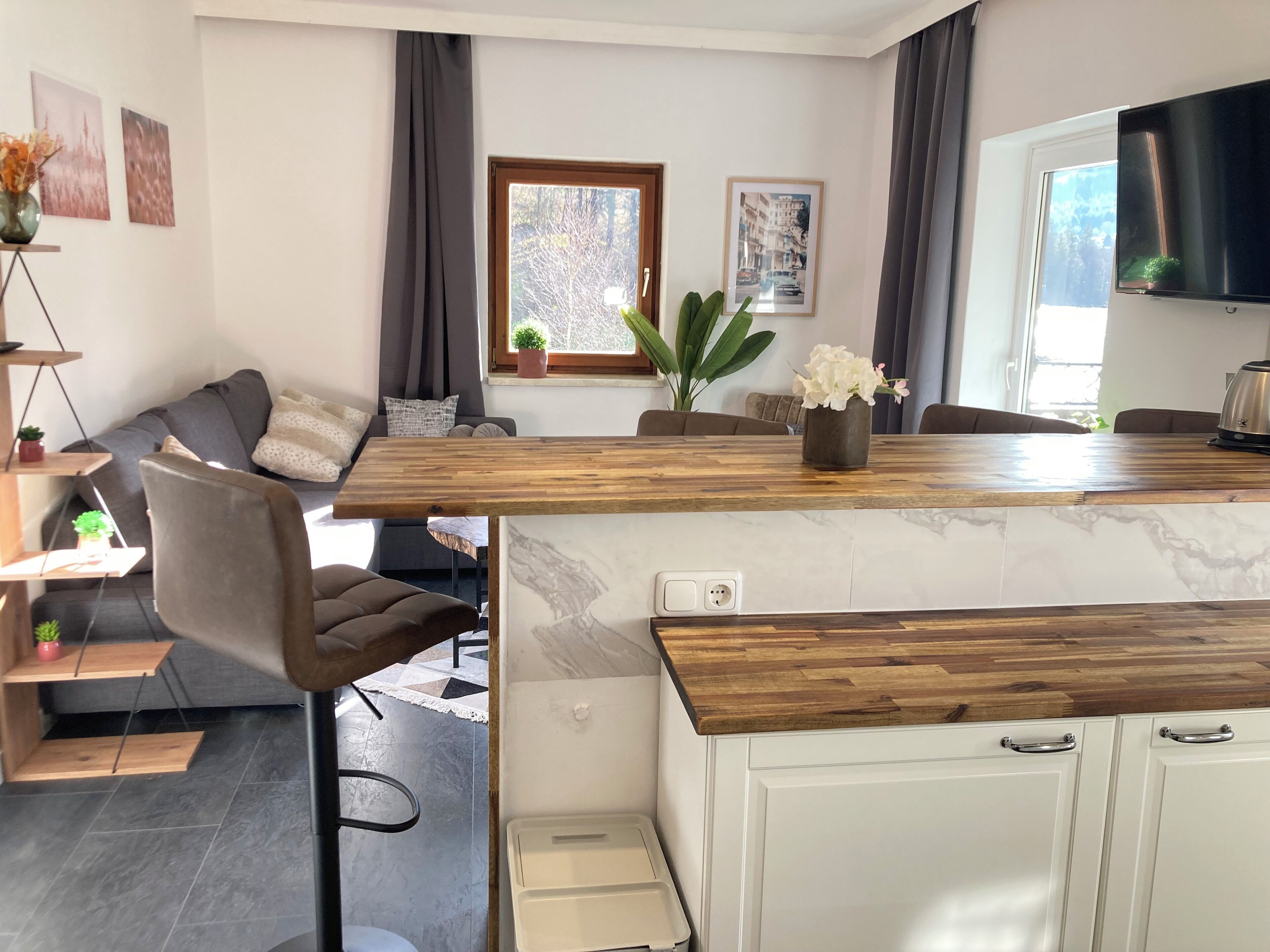 Eine moderne Küche mit Holzarbeitsplatte, weißen Schränken und einem eingebauten Backofen. Es gibt einen Essbereich mit einer grauen Couch und einem kleinen Tisch.