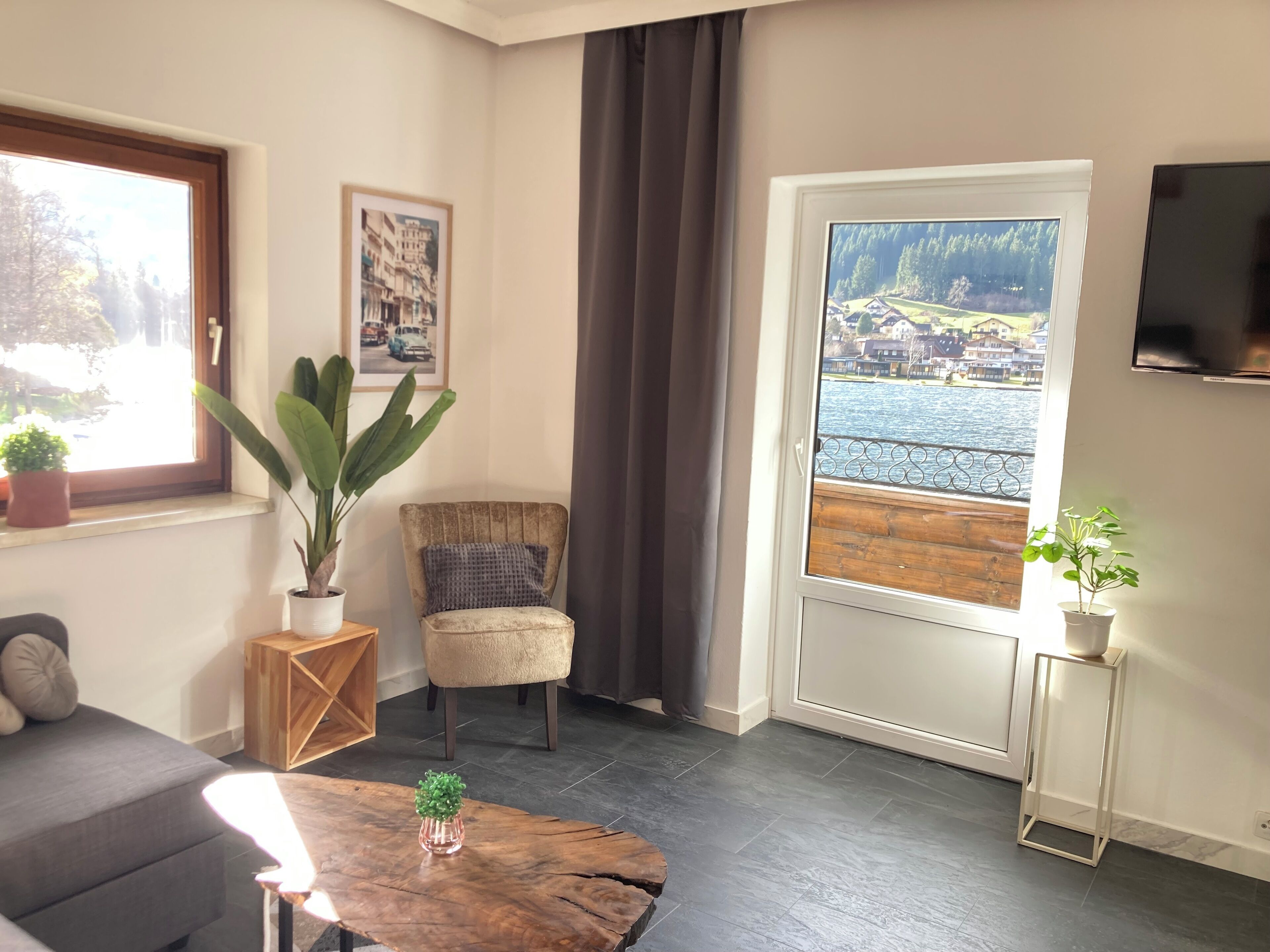 A living room with a view of a lake, a sofa, a chair, a coffee table, and a TV.