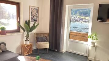 A living room with a view of a lake, a sofa, a chair, a coffee table, and a TV.