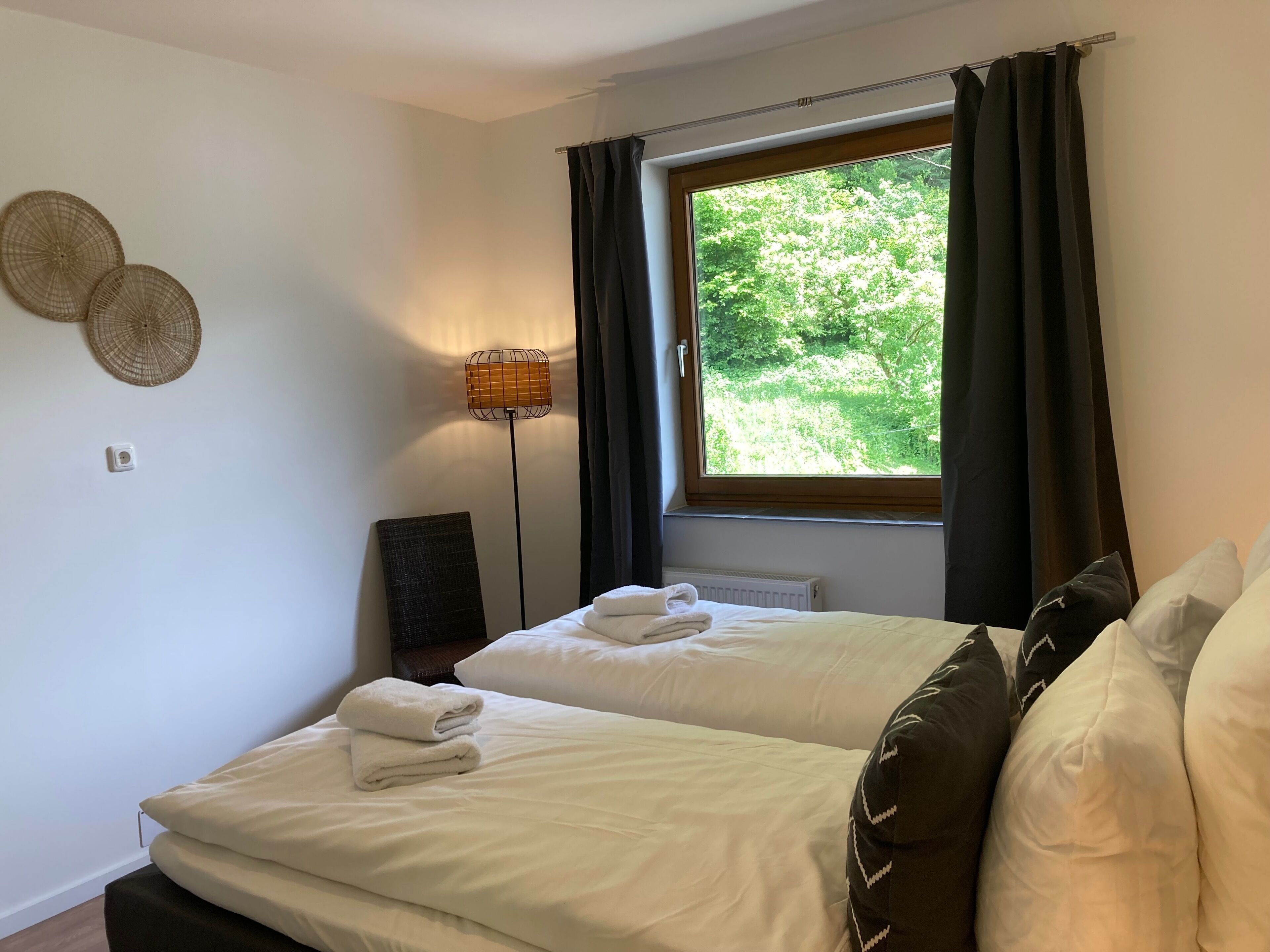A hotel room with two beds, a window with curtains, a standing lamp, and wall decor.