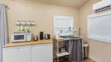 Una kitchenette compacta con microondas, cafetera y un lavamanos pequeño.